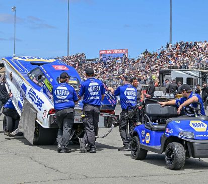 NAPA Auto Care crew towing their funny car through the pits behind a golf cart